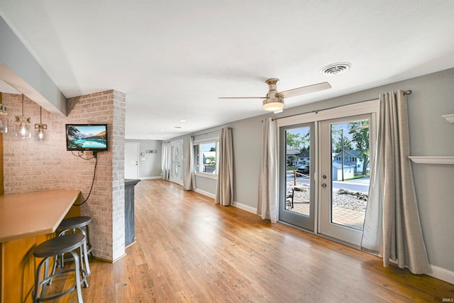 unfurnished living room with ceiling fan, brick wall, hardwood / wood-style flooring, and french doors