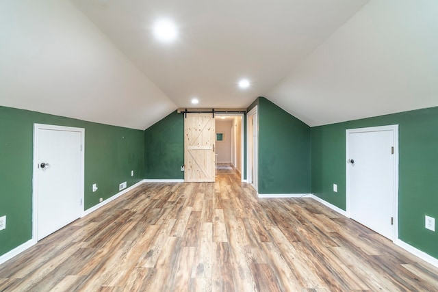 additional living space with lofted ceiling, hardwood / wood-style flooring, and a barn door