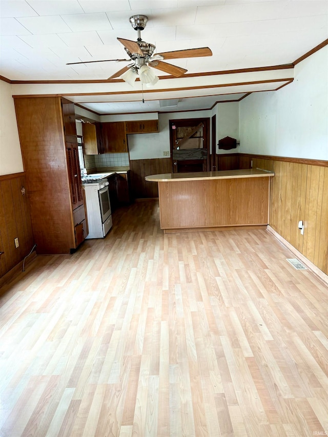 kitchen featuring kitchen peninsula, white gas range oven, wood walls, and light wood-type flooring