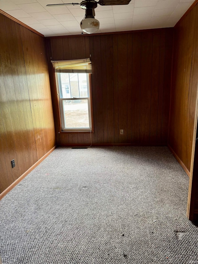 empty room with carpet, wooden walls, and ceiling fan