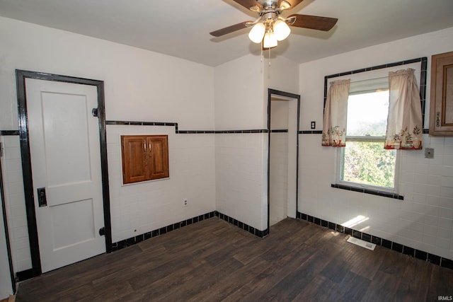 unfurnished bedroom featuring tile walls, dark hardwood / wood-style flooring, and ceiling fan