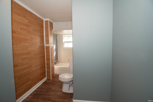 bathroom featuring wooden walls, hardwood / wood-style flooring, tiled shower / bath, and toilet