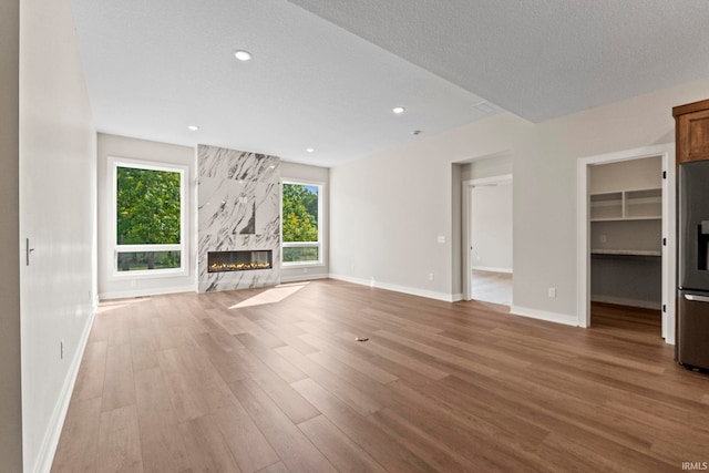 unfurnished living room with a premium fireplace, a textured ceiling, and light hardwood / wood-style flooring