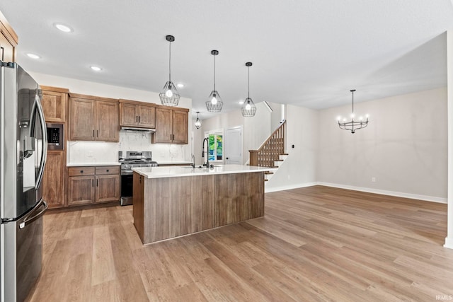 kitchen featuring appliances with stainless steel finishes, a kitchen island with sink, decorative light fixtures, an inviting chandelier, and light hardwood / wood-style flooring