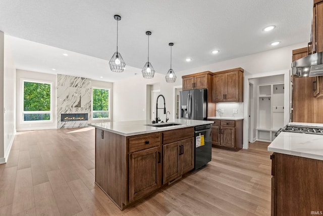 kitchen featuring appliances with stainless steel finishes, sink, decorative light fixtures, a center island with sink, and a fireplace