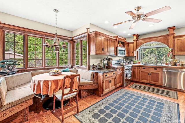 kitchen with ceiling fan with notable chandelier, stainless steel appliances, light hardwood / wood-style flooring, decorative light fixtures, and sink