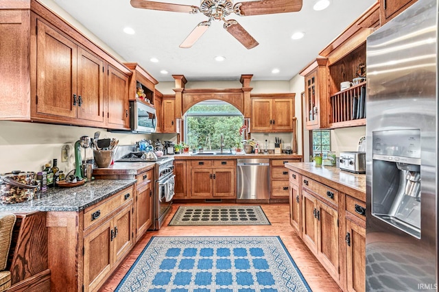 kitchen with dark stone counters, light hardwood / wood-style floors, sink, stainless steel appliances, and ceiling fan