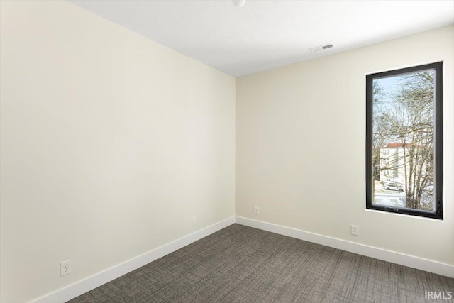 unfurnished room with a healthy amount of sunlight, dark carpet, and baseboards