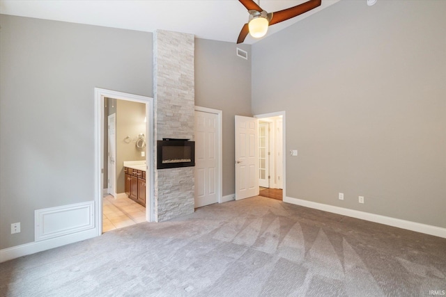 interior space with a fireplace, a high ceiling, visible vents, ceiling fan, and light colored carpet