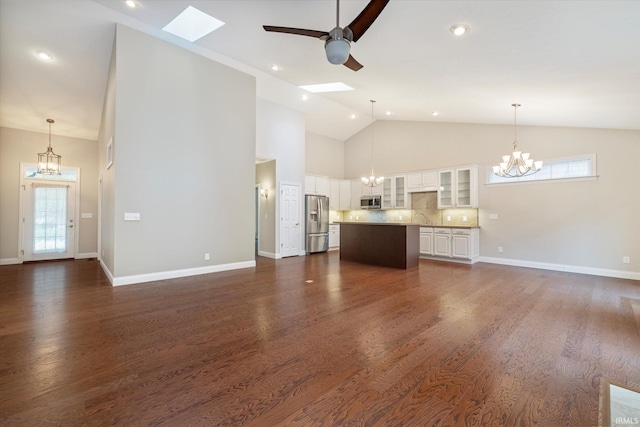 unfurnished living room with dark wood-style flooring, baseboards, a skylight, high vaulted ceiling, and ceiling fan with notable chandelier