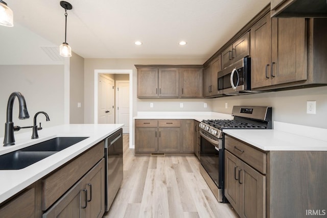 kitchen with pendant lighting, sink, light wood-type flooring, appliances with stainless steel finishes, and dark brown cabinetry