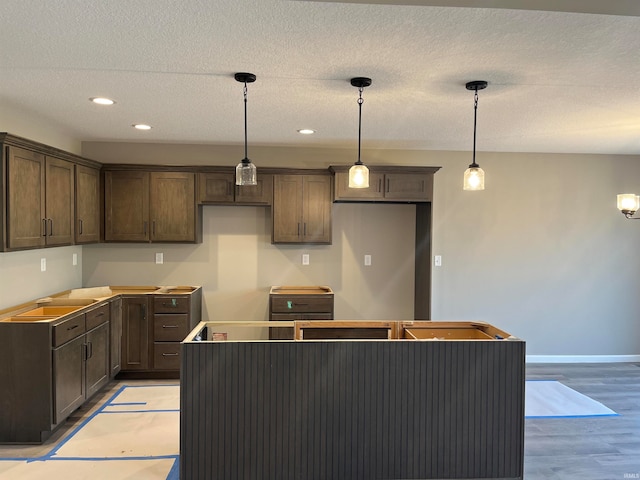 kitchen with a textured ceiling, light hardwood / wood-style flooring, hanging light fixtures, and dark brown cabinets