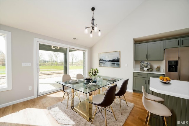 dining area featuring high vaulted ceiling, a chandelier, light hardwood / wood-style flooring, and plenty of natural light