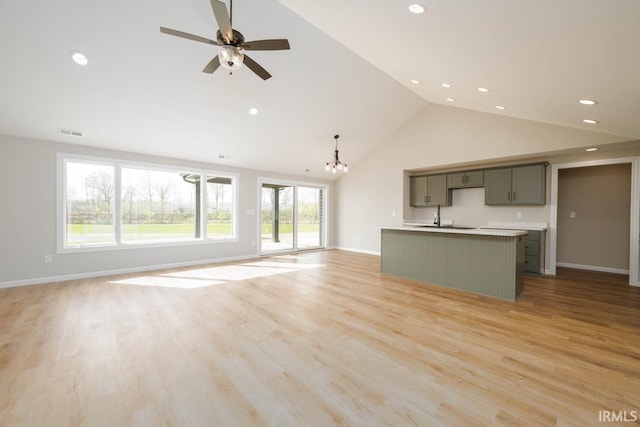 unfurnished living room with high vaulted ceiling, light wood-type flooring, ceiling fan with notable chandelier, and sink