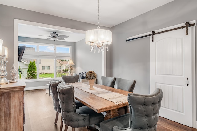 dining space with ceiling fan with notable chandelier, hardwood / wood-style flooring, and a barn door