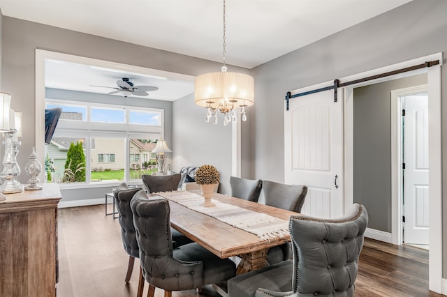 dining area featuring dark hardwood / wood-style flooring, ceiling fan with notable chandelier, and a barn door