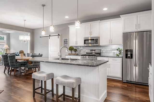 kitchen with dark hardwood / wood-style flooring, stainless steel appliances, a center island with sink, and a barn door