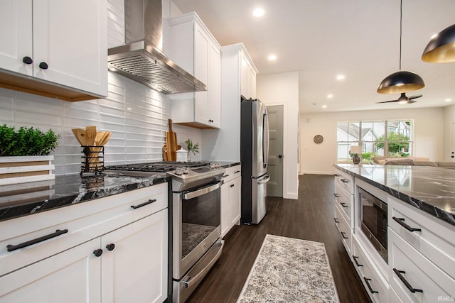 kitchen featuring dark stone counters, white cabinetry, appliances with stainless steel finishes, and wall chimney range hood