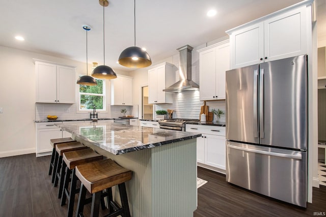 kitchen featuring a kitchen island, white cabinetry, appliances with stainless steel finishes, and wall chimney range hood