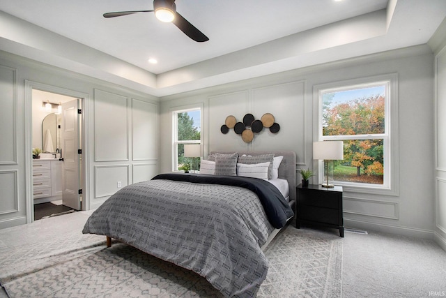 carpeted bedroom with ceiling fan, a raised ceiling, and ensuite bathroom