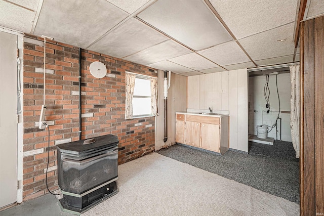 living room with carpet flooring, sink, a wood stove, brick wall, and a drop ceiling