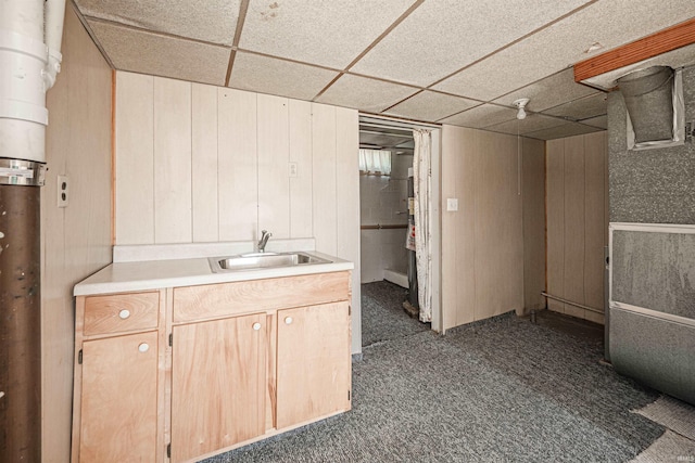 basement with wood walls, dark colored carpet, a paneled ceiling, and sink