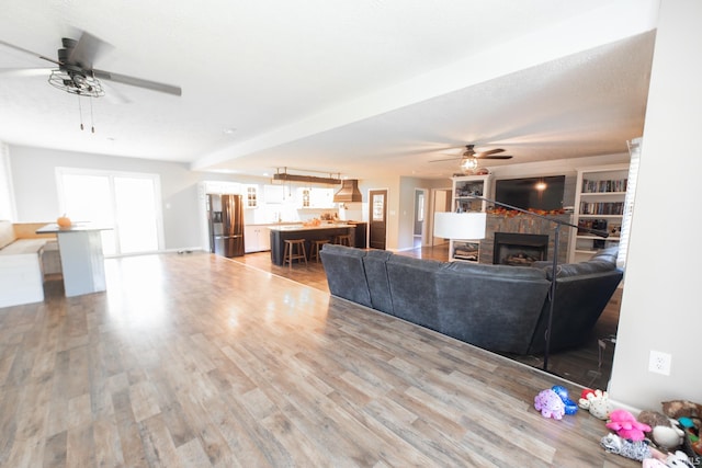 living room featuring ceiling fan, a stone fireplace, and hardwood / wood-style flooring