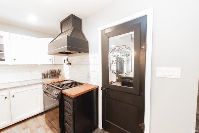 kitchen with stainless steel stove, custom exhaust hood, light hardwood / wood-style flooring, and white cabinetry