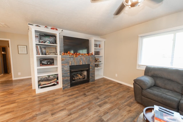 living room with a textured ceiling, a stone fireplace, hardwood / wood-style floors, and ceiling fan