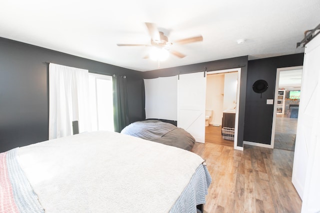 bedroom with ceiling fan, light hardwood / wood-style floors, ensuite bath, and a barn door