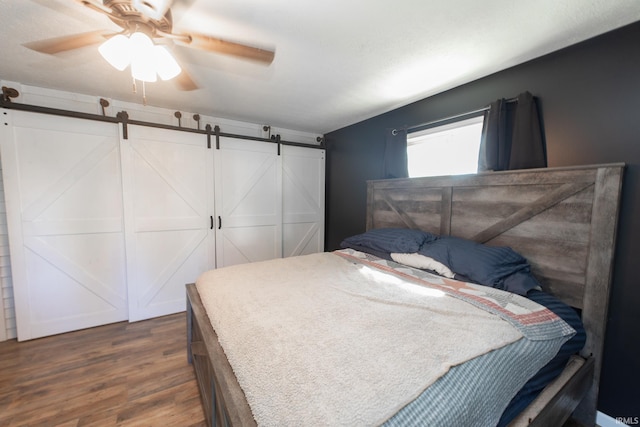 bedroom featuring ceiling fan, dark hardwood / wood-style floors, and a barn door