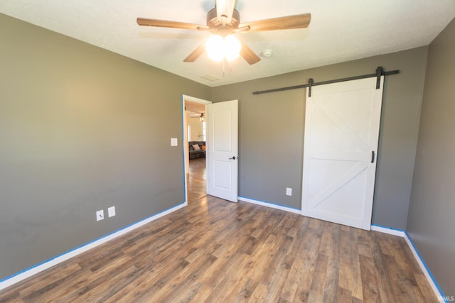 unfurnished bedroom featuring a barn door, a textured ceiling, dark hardwood / wood-style flooring, and ceiling fan