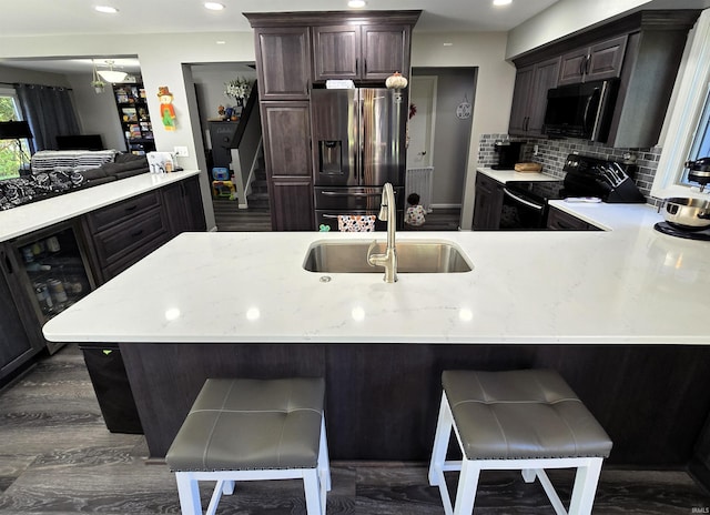 kitchen with kitchen peninsula, backsplash, a breakfast bar, sink, and black appliances