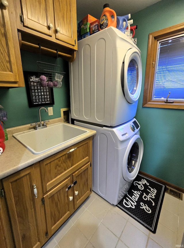 laundry room with cabinets, light tile patterned floors, stacked washer and clothes dryer, and sink