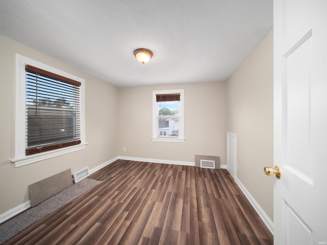 spare room featuring a textured ceiling and dark hardwood / wood-style flooring