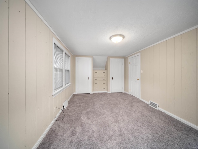 carpeted empty room with a textured ceiling and wooden walls