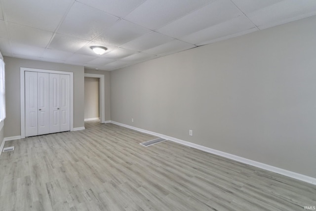 unfurnished bedroom with light wood-type flooring, a closet, and a paneled ceiling