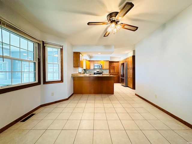 kitchen featuring backsplash, kitchen peninsula, appliances with stainless steel finishes, and light tile patterned flooring