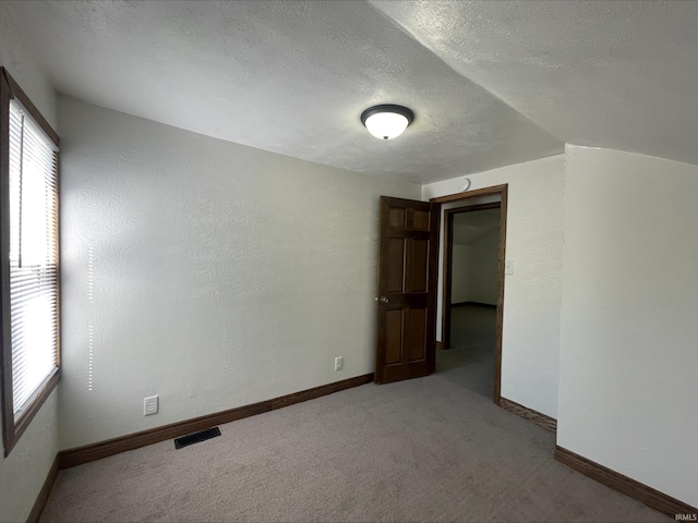 unfurnished room with carpet, vaulted ceiling, and a textured ceiling