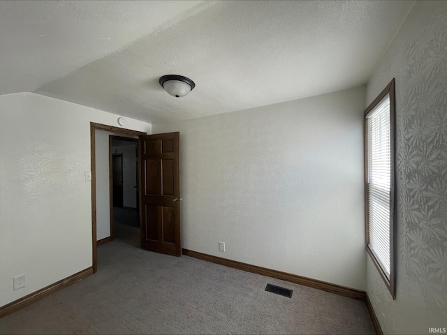 carpeted empty room featuring vaulted ceiling and a textured ceiling