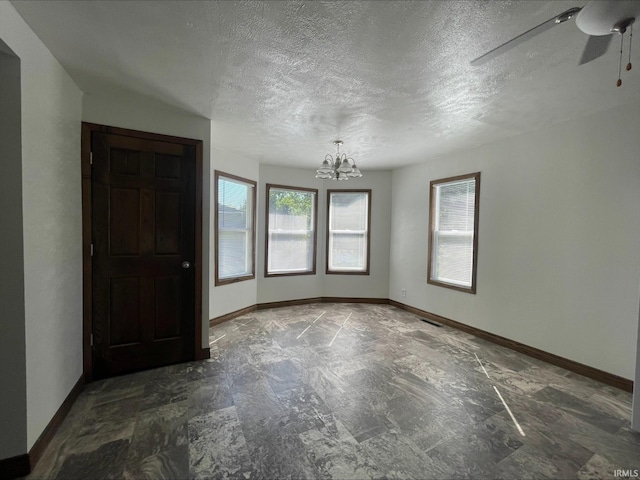 empty room with ceiling fan with notable chandelier and a textured ceiling