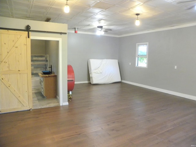 basement featuring ceiling fan, a barn door, and dark hardwood / wood-style flooring