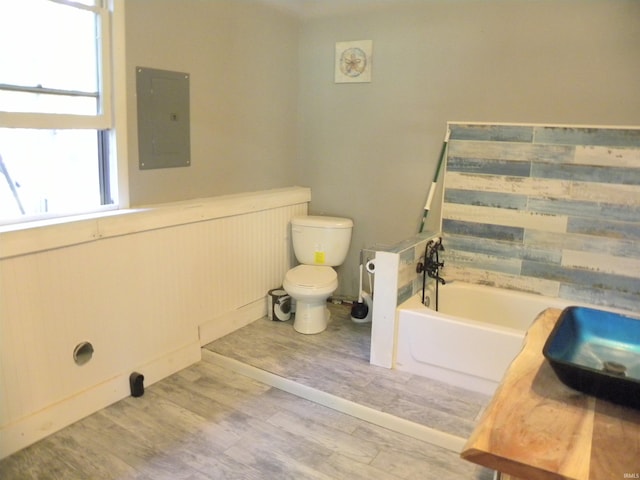 bathroom with electric panel, wood-type flooring, a tub, toilet, and sink