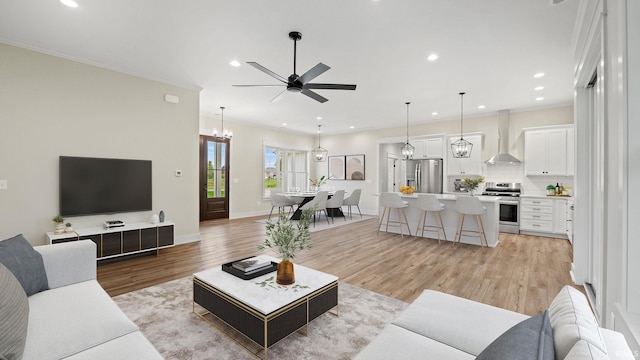 living room featuring light wood-type flooring, ceiling fan with notable chandelier, and ornamental molding