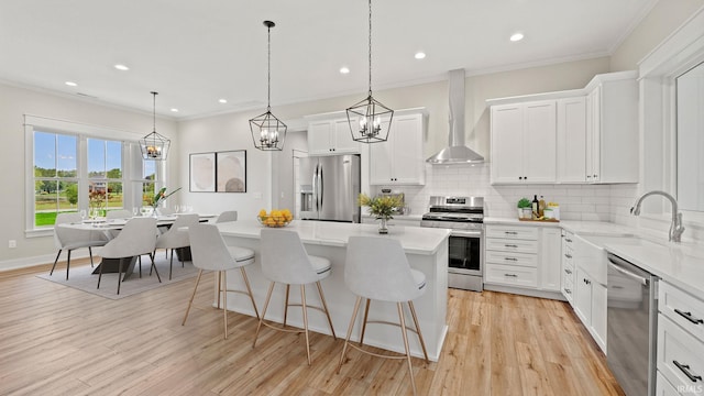 kitchen featuring pendant lighting, a kitchen island, wall chimney exhaust hood, white cabinetry, and appliances with stainless steel finishes