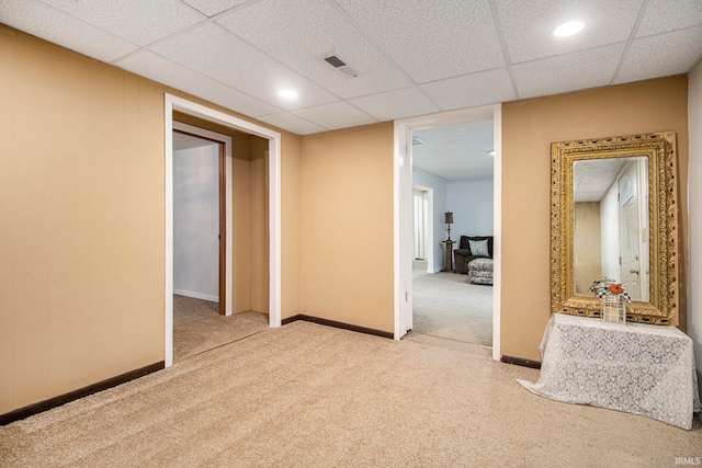 interior space with a paneled ceiling and light carpet