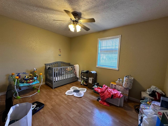 bedroom with ceiling fan, a crib, light wood-type flooring, and a textured ceiling