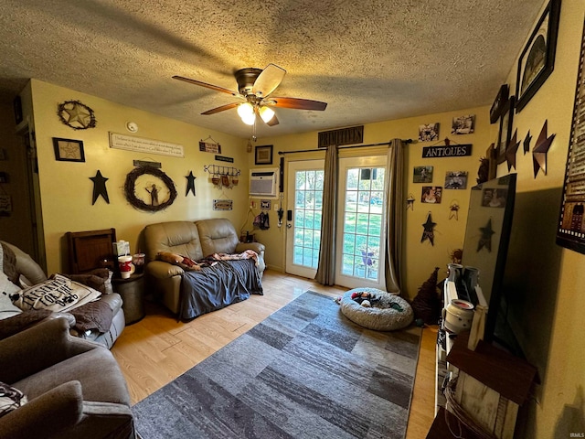 living room with a wall unit AC, ceiling fan, light hardwood / wood-style flooring, and a textured ceiling