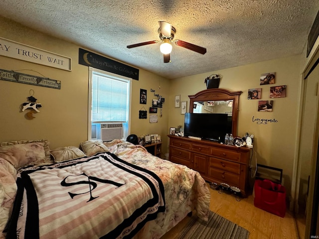 bedroom featuring ceiling fan, cooling unit, light hardwood / wood-style floors, and a textured ceiling