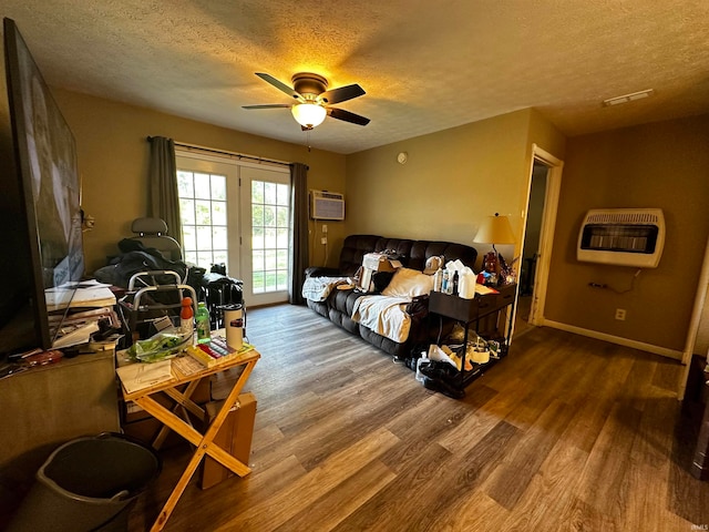 living room with ceiling fan, a wall unit AC, heating unit, wood-type flooring, and a textured ceiling